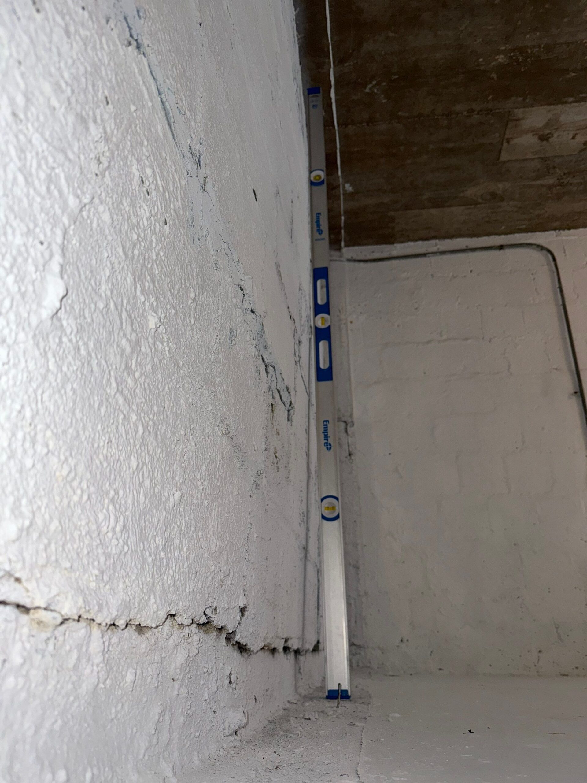 Level tool showing bowing and horizontal crack in painted basement wall