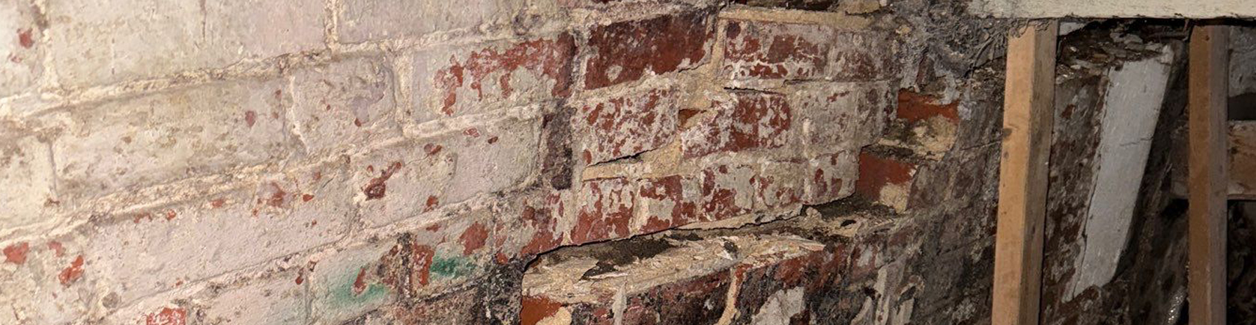 Basement foundation wall with crumbling bricks, mortar deterioration, and visible structural damage requiring repair.
