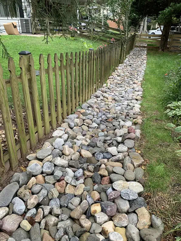 New exterior drainage system with French drain and decorative stone channel in residential backyard in Alexandria VA